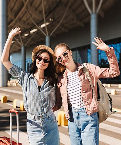 Ventajas para Particulares - Dos jóvenes sonriendo y felices con maletas en el aeropuerto