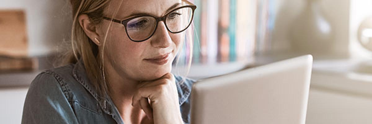 Seguro de Proteccion de Pagos - Mujer con gafas sentada en la cocina de su casa con una tablet en la mano y papeles sobre la mesa, trabajando online Seguro de Proteccion de Pagos - Mujer con gafas sentada en la cocina de su casa con una tablet en la mano y papeles sobre la mesa, trabajando online